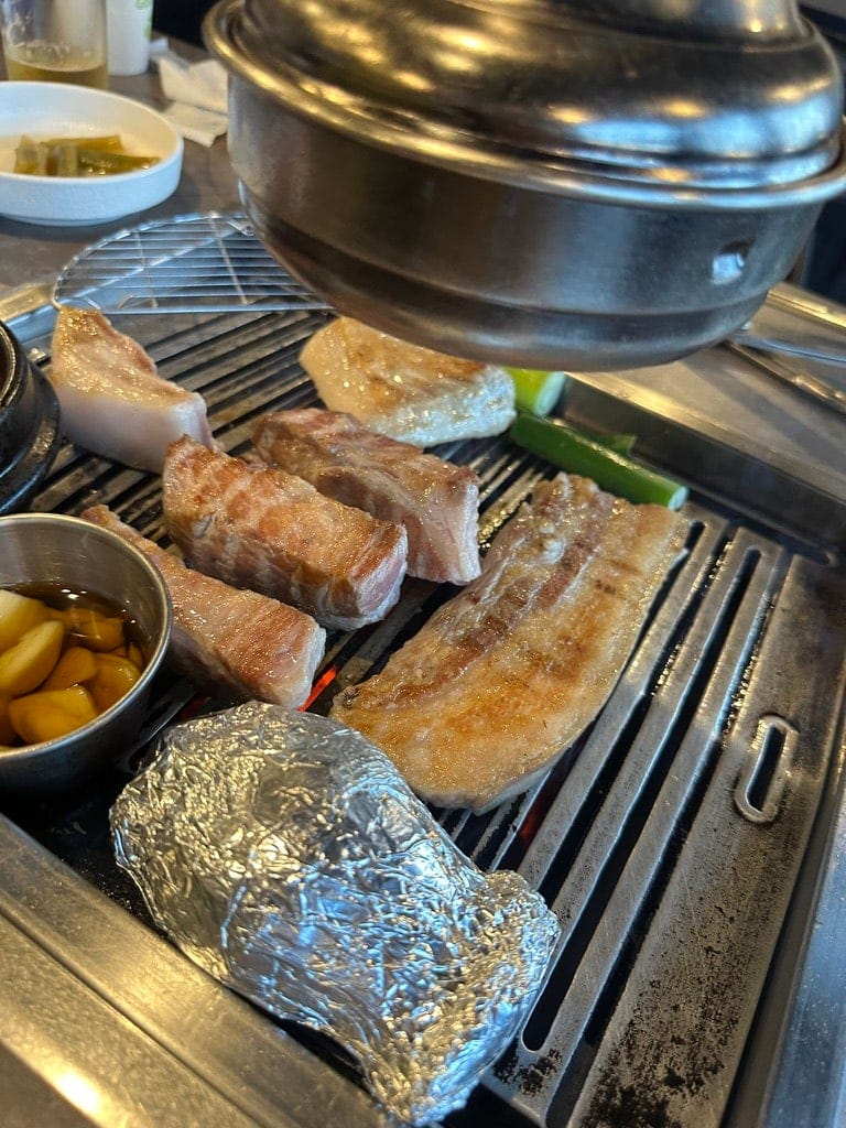 Black pork belly and neck on the grill at Godokan, with a stew pot at the side