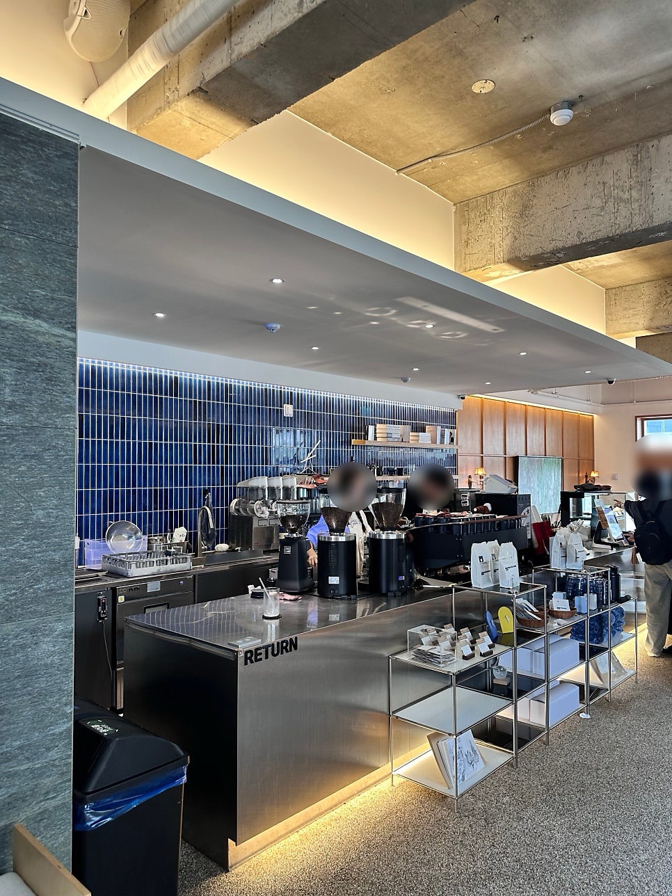 Bar counter at Joogiyul with blue tiles, a stainless steel counter marked RETURN and coffee bean packages on shelves