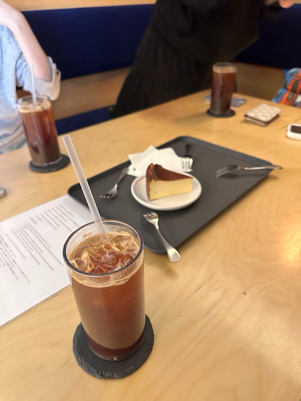 Iced americano on a slate coaster and a slice of Basque cheesecake on a tray at Joogiyul
