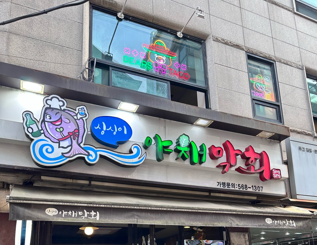Exterior of Singsingi Yachae Makhoe in Gangnam with a cartoon fish mascot sign